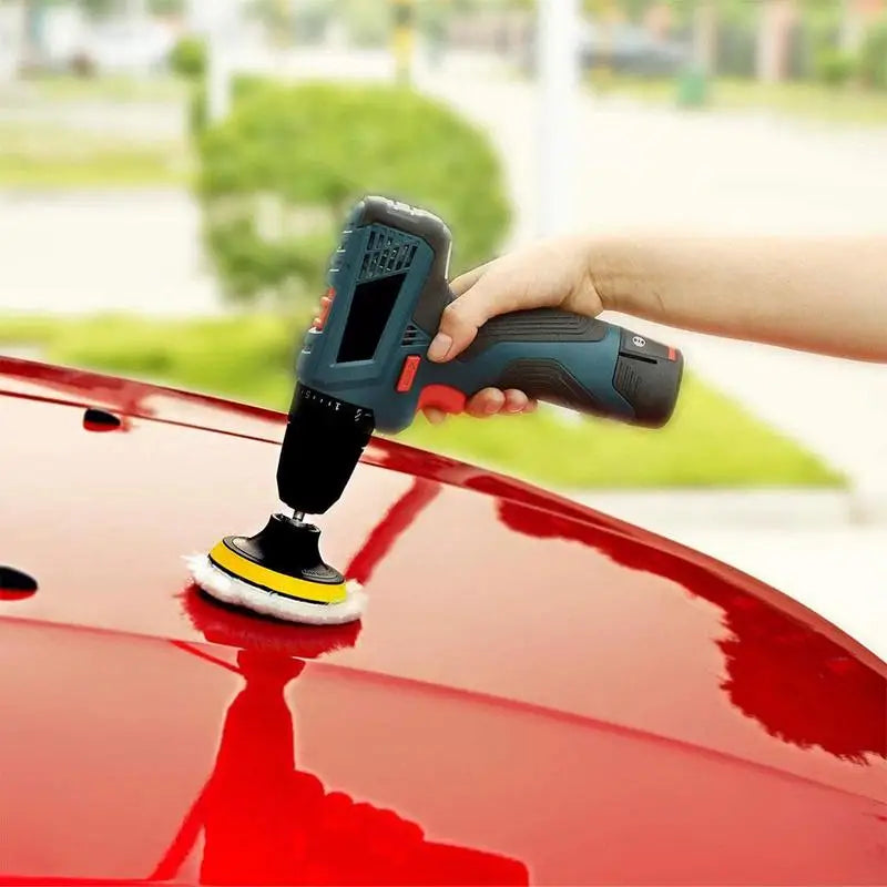 Hand using cordless car buffer polisher on a red car hood.