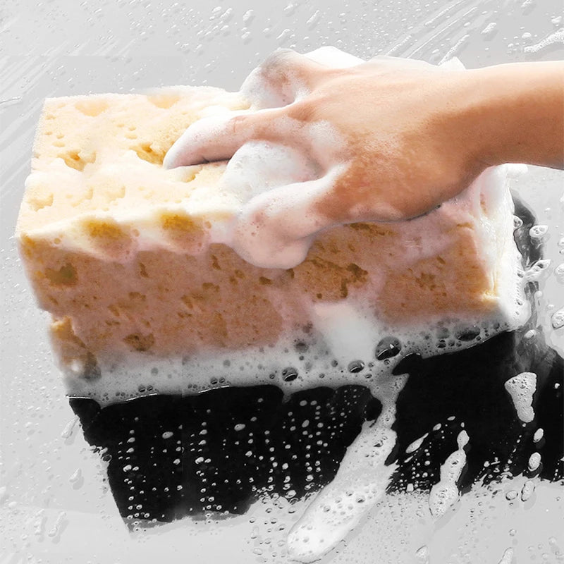 Hand cleaning a surface with a soapy yellow sponge.