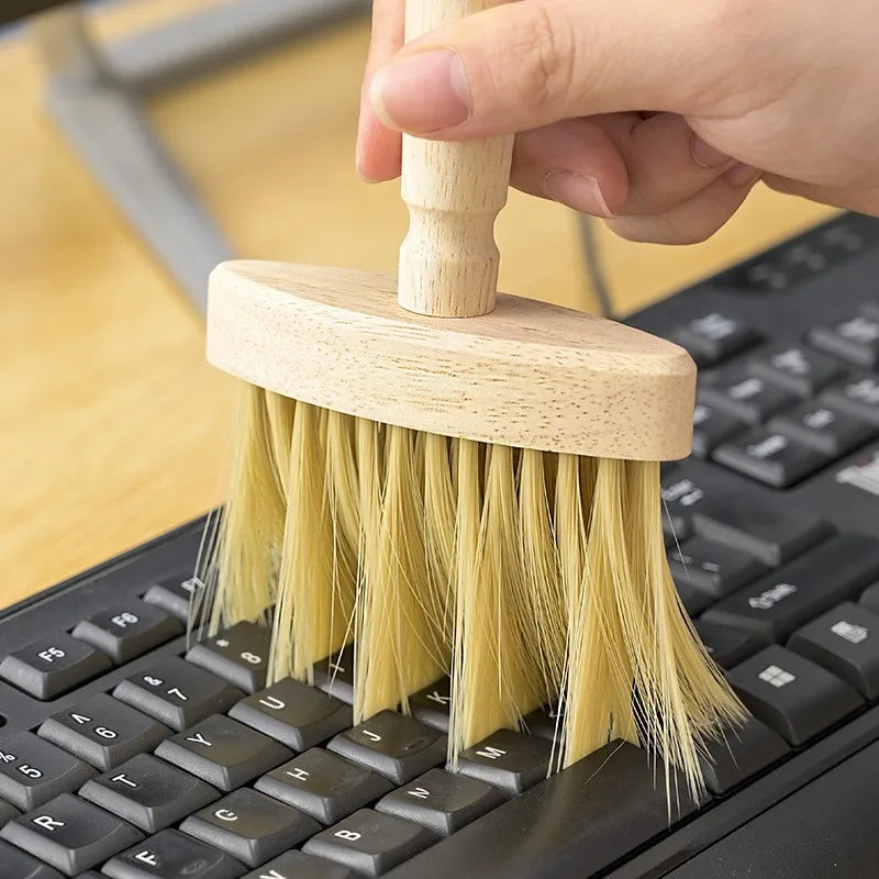 Wooden keyboard cleaning brush dusting a black computer keyboard.