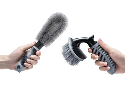Two hands holding car detailing brushes: a long-handled brush and a hand-held brush.