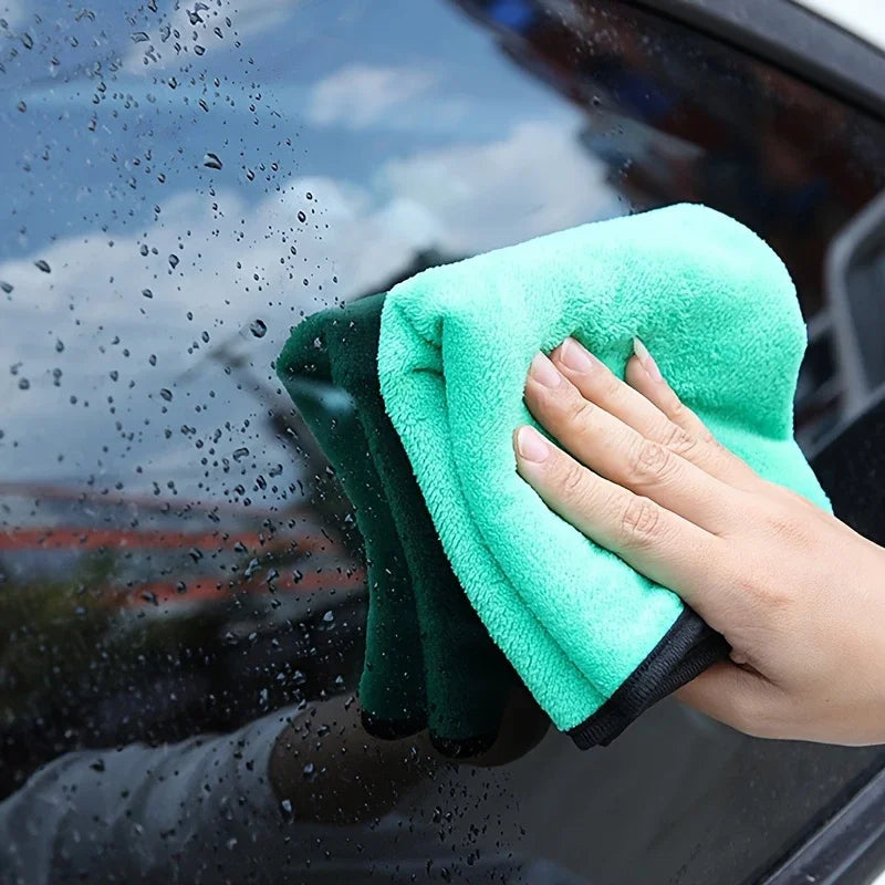 Green microfiber towel cleaning a car windshield.