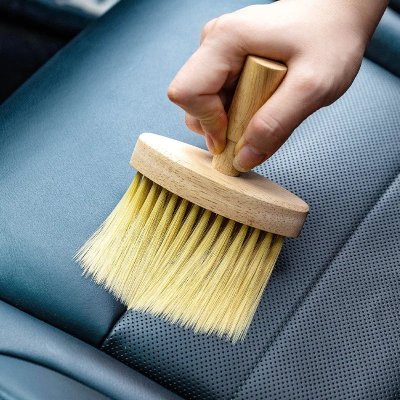Hand using wooden brush to clean perforated blue leather car seat.