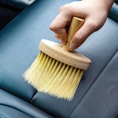 Hand using wooden brush to clean perforated blue leather car seat.