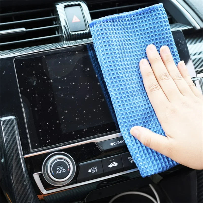 Blue waffle weave microfiber cloth cleaning a car's dashboard screen.