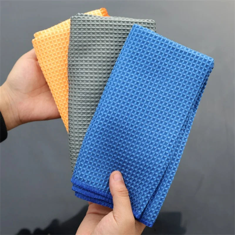 Hand holding waffle weave microfiber cloths in orange, gray, and blue.