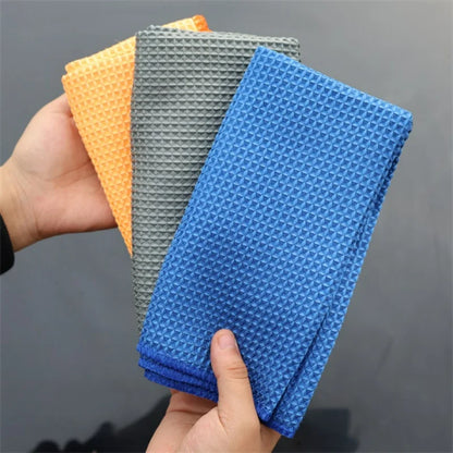 Hand holding waffle weave microfiber cloths in orange, gray, and blue.