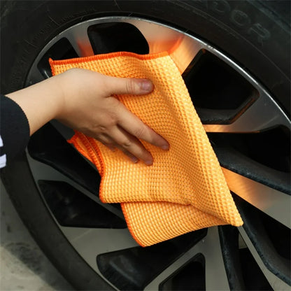 Orange microfiber towel cleaning a car wheel.