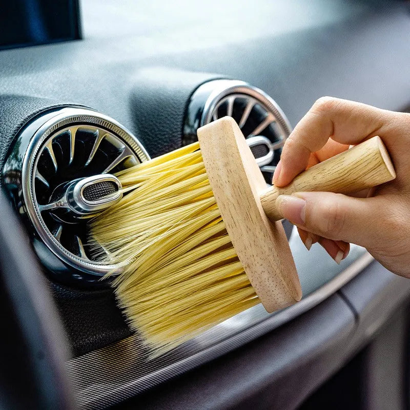 Hand using car detailing brush to clean a car air vent. Wooden handle and yellow bristles.