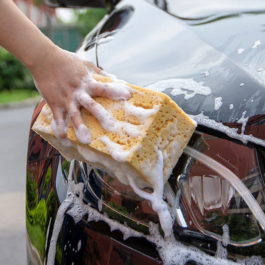 Hand washing a black car with a soapy yellow sponge, showcasing car detailing.