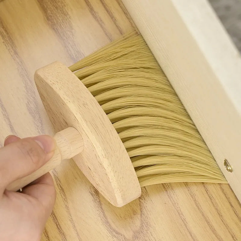 Hand holding a wooden brush sweeping across a light wooden surface, close-up view.
