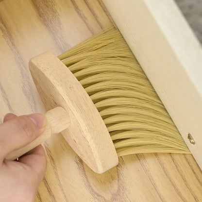 Hand holding a wooden brush sweeping across a light wooden surface, close-up view.