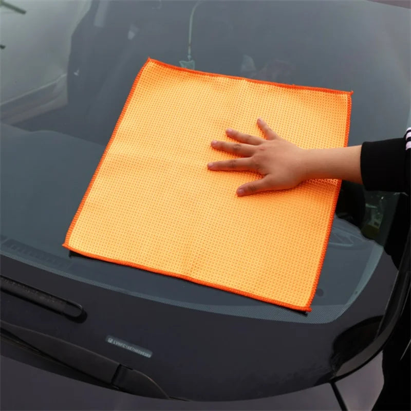 Orange microfiber cleaning cloth on car windshield, hand wiping.