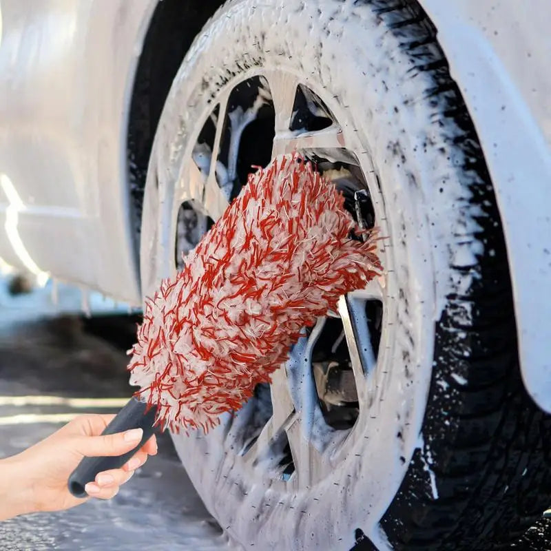 Cleaning car wheels with a red and white wheel brush and soap.